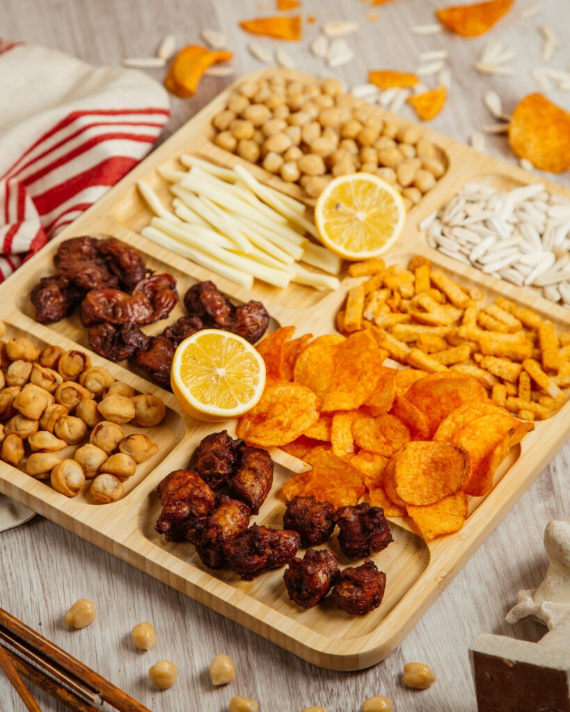 top view of assorted beer snacks as fried dushbara grilled chicken cheese boiled chickpeas and potato chips on a wooden board